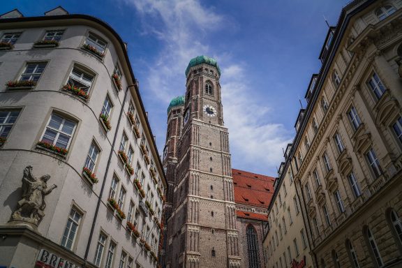 Blick auf die Türme der Frauenkirche in München, umgeben von historischen Gebäuden.